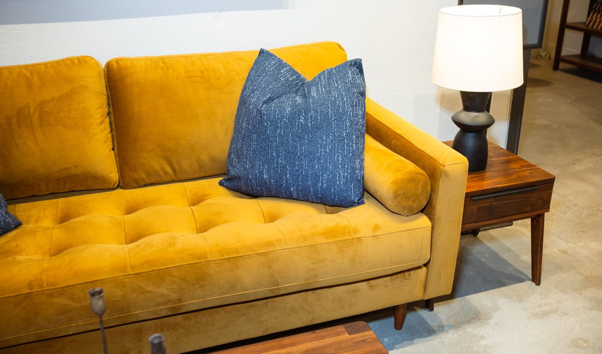 A mustard velvet sofa with a tufted seat and a bolster pillow in What's New Furniture's Cedar Mill showroom