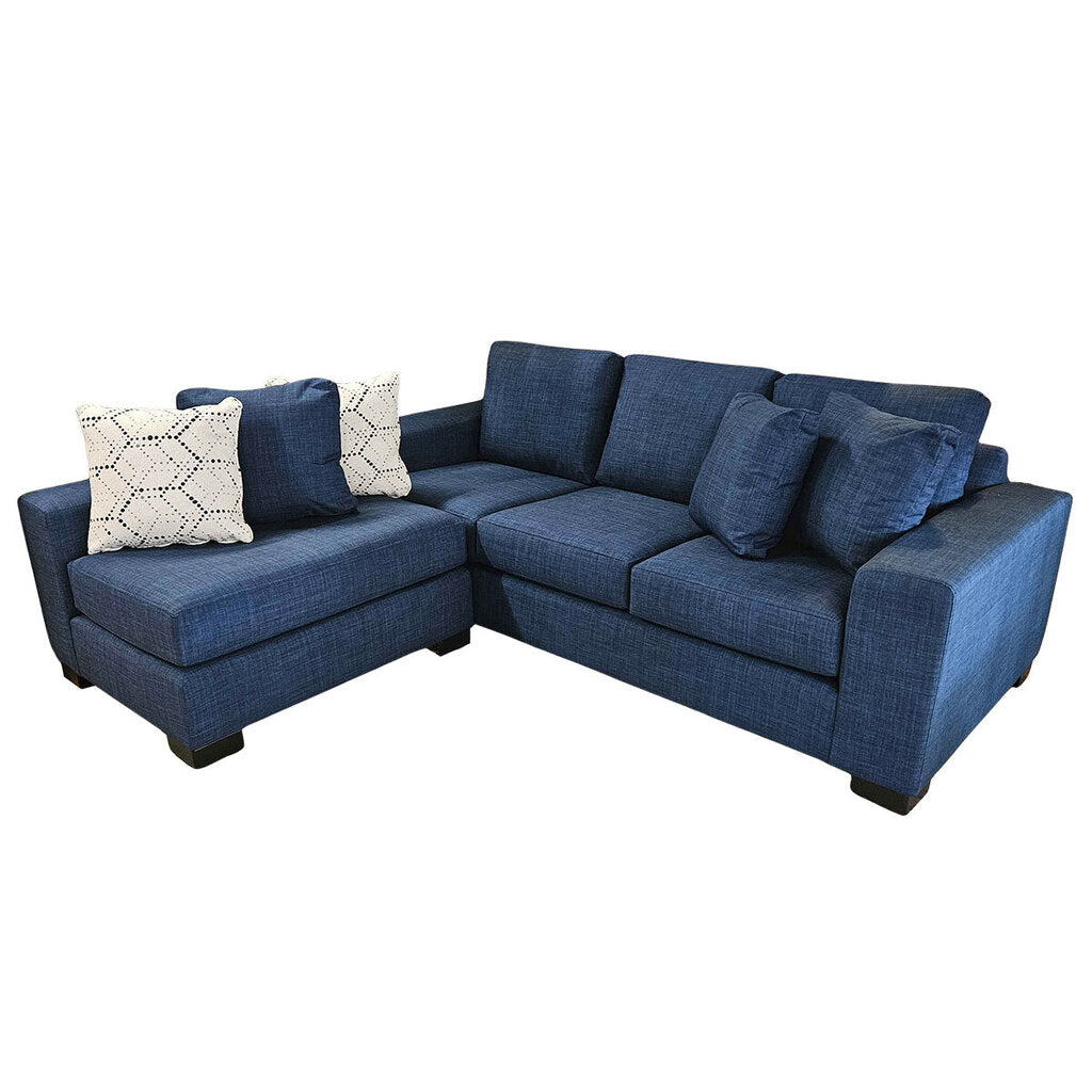 A reversible sectional sofa in indigo color with a chaise on the left side, accompanied by two patterned pillows.