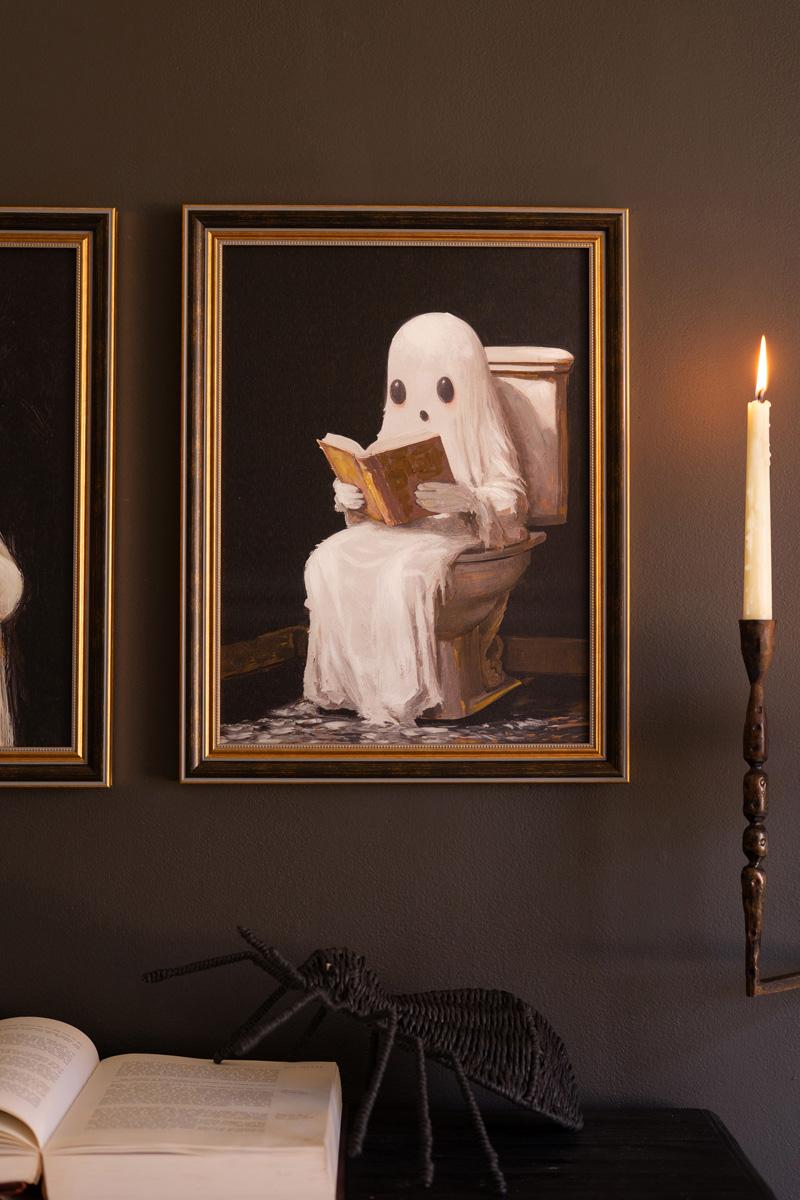 Framed painting of a ghost reading a book while sitting on a toilet, lit by a taper candle - ghost wall art by Kalalou - Whats New Furniture Portland OR