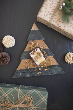 Christmas tree cutting board in green marble and acacia shown on a black surface beside wrapped gifts - holiday serveware by Kalalou - Whats New Furniture Portland OR