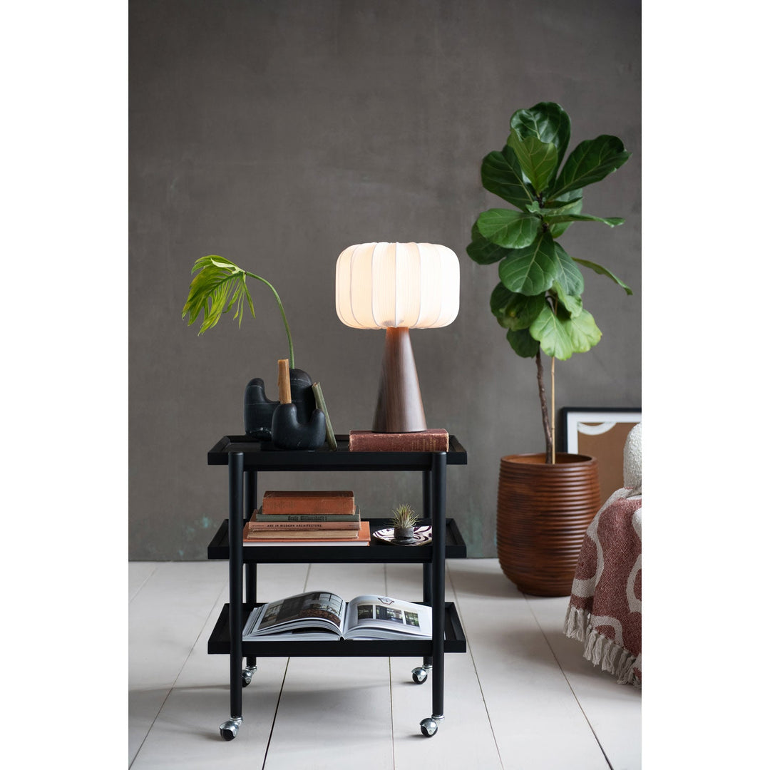 Wood finish pleated shade lamp lit on a shelf beside a potted plant in a grey-walled Portland room - Whats New Furniture Portland OR