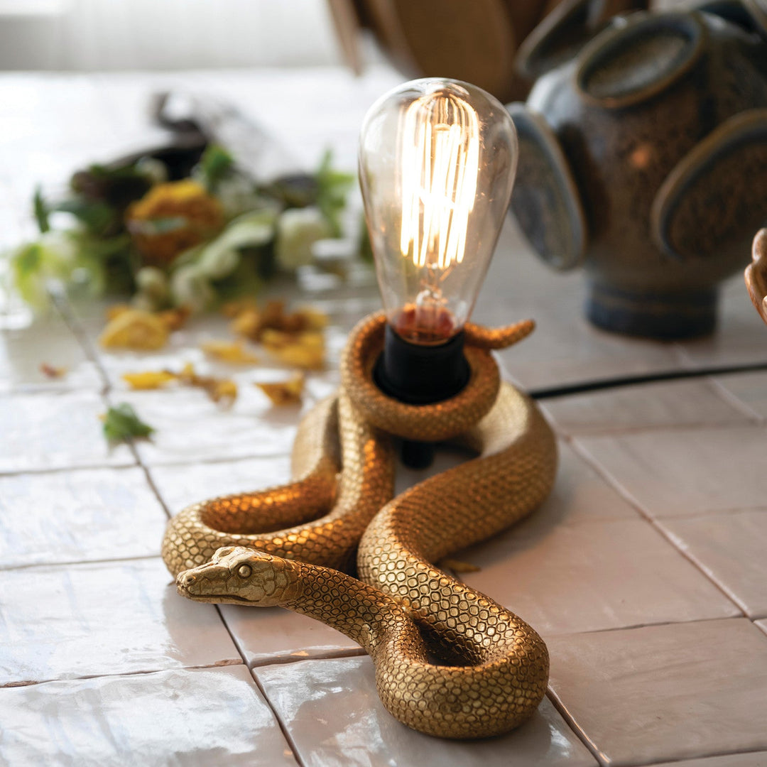 Gold snake table lamp styled lit on a terracotta tile floor with dried botanicals and pottery in a Portland home - Whats New Furniture