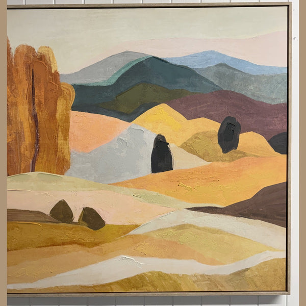 Framed desert landscape painting with an orange bluff in a light wood floater frame, hung in the What's New Furniture showroom