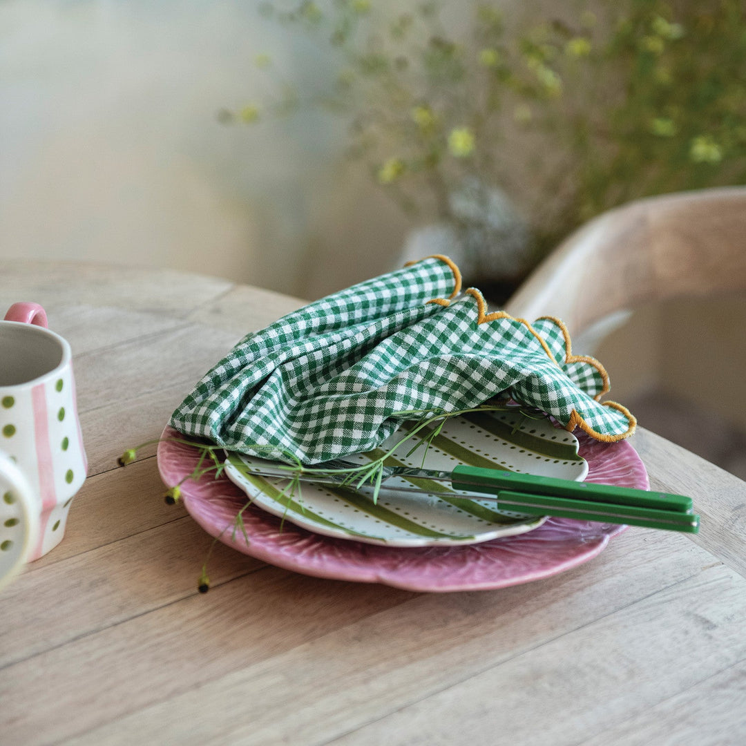 Green check scalloped napkins styled on a dining table with pink plates