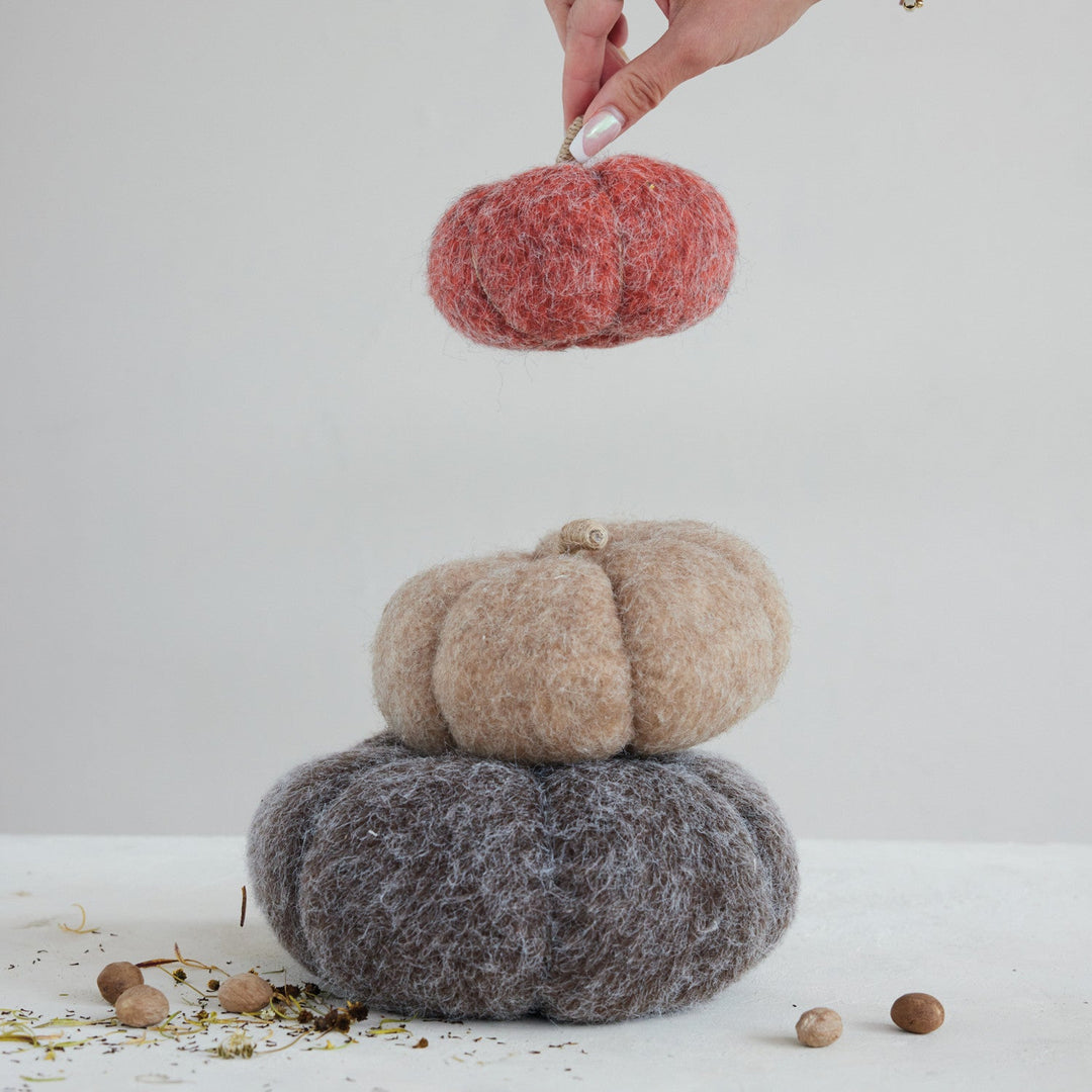 Felt pumpkin trio styled stacked with the grey 8.5-inch pumpkin at the base and a hand placing the orange one on top - Whats New Furniture Portland