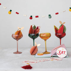 Four colored coupe glasses styled under a felt holiday garland with paper ornaments - Creative Co-Op stemware - Whats New Furniture Portland