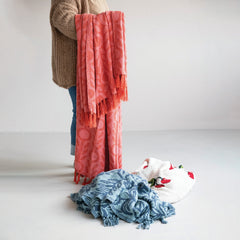 Pink floral jacquard throw styled held up showing drape and fringe with more throws piled below in a Portland studio - Whats New Furniture
