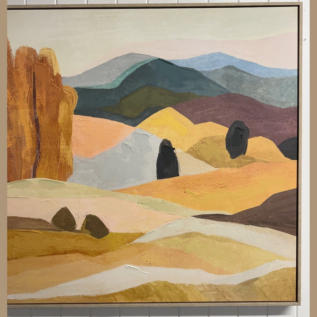 Framed desert landscape painting with an orange bluff in a light wood floater frame, hung - What's New Furniture showroom