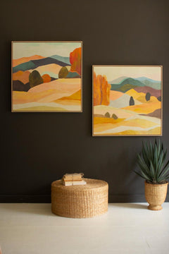 Framed desert landscape painting with an orange bluff in a light wood floater frame — shown hanging alongside its companion pieces