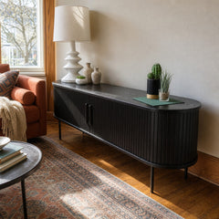 Black fluted oak TV lowboard styled in a living room beneath a window with a lamp and plants
