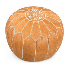 Tan round pouf ottoman with a low cylindrical silhouette.