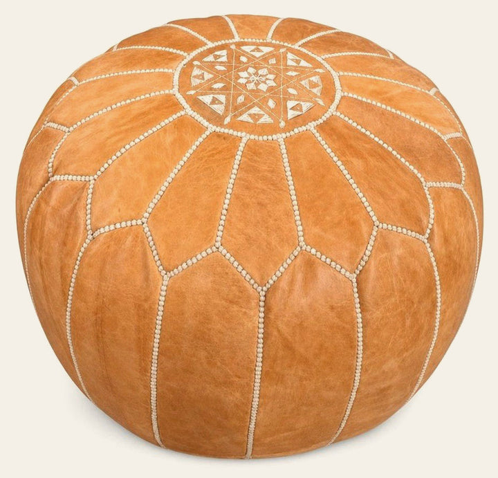 Tan round pouf ottoman with a low cylindrical silhouette.