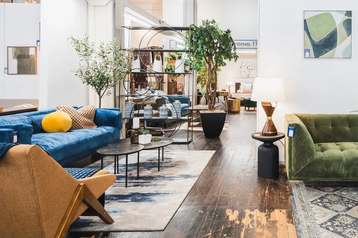 The showroom floor at What's New Furniture in Portland: a blue velvet sofa, a woven lounge chair, a green tufted sofa and rugs on worn wood floors