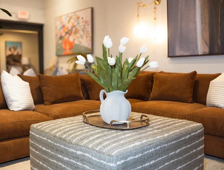 A rust velvet sectional with a striped ottoman and white tulips in the Cedar Mill showroom