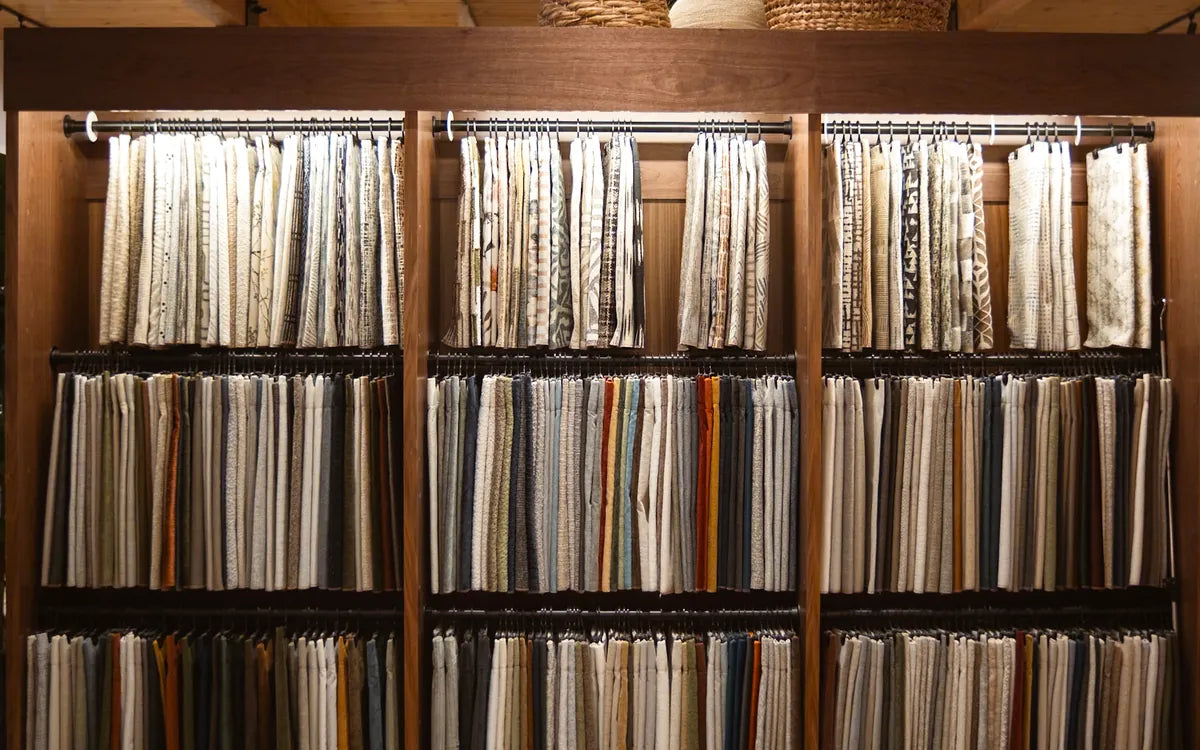 Three bays of hanging fabric samples on walnut shelving in our Cedar Mill fabric library - Whats New Furniture Portland