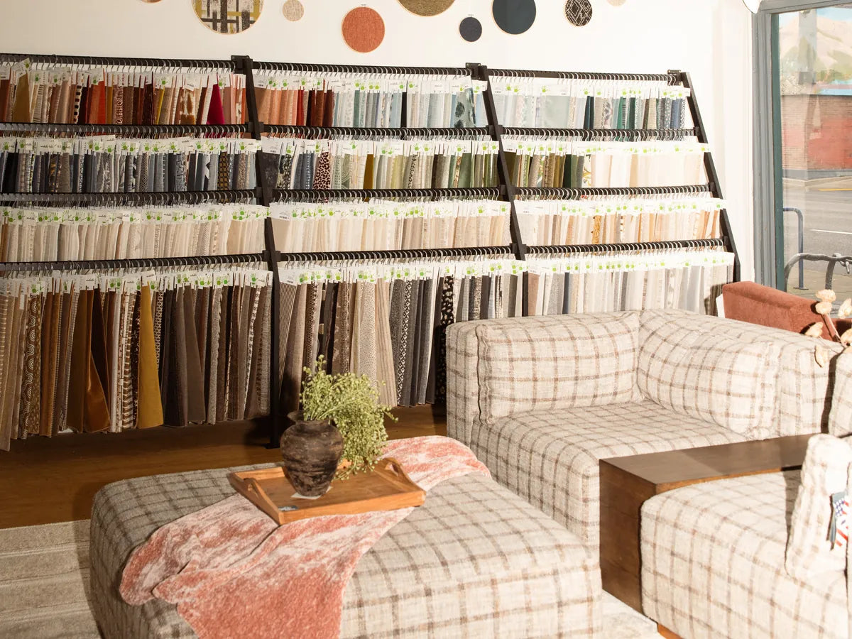 Rows of hanging fabric samples on the fabric wall at our Portland store, with a plaid sectional and ottoman in front